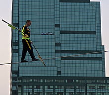 A man tightrop walks with a large building in the background