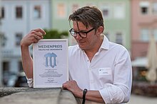 Thilo Schmidt präsentiert nach der Verleihung des Medienpreises Vielfältige Demokratie 2023 seine Urkunde auf dem Marktplatz in Pirna