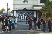 Image de personne devant une affiche promotionnelle pour un concert de Nightwish