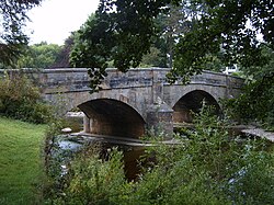 A three-arch bridge spanning a river, surrounded by trees