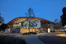 View of the Studio Art Hall, a contemporary gray building consisting of modules unified by an undulating roof, illuminated at dusk