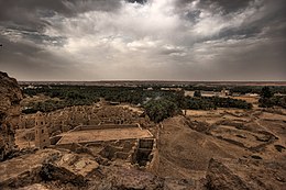 Ruins of a desert oasis town with palm groves in the background