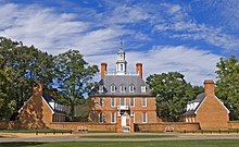 A three-story red brick colonial style hall and its left and right wings during summer.