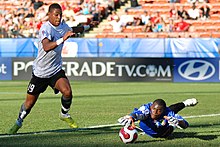 Un gardien de foot arrêtant un ballon tandis que le buteur se remet de son coup de pied.