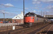 A passenger train with a streamlined diesel locomotive next to a modern brick station building