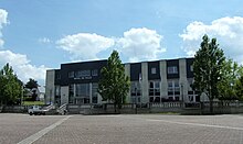 Photographie en couleurs d'un vaste bâtiment récent portant en façade l'inscription « Hôtel de ville ».