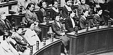 Photo noir et blanc de trois rangeés de pupitres d'un parlement devant lesquels sont assises des femmes.