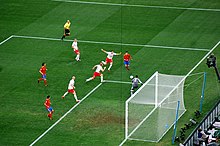 Vue de huit joueurs se disputant le ballon devant le but et de l'arbitre pendant un match de football