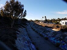 A creek in a concrete channel that has been decorated with graffiti.