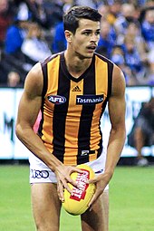 Male athlete in sleeveless guernsey holds football