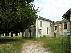 Photographie en couleurs d'un ensemble de bâtiments à demi dissimulés derrière un arbre.