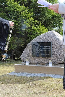 Taustal fookuses tumedast grandiisit mälestuskivi, esiplaanil õigeusu preester suitsutiga (vasakul) ja kõnepidaja (paremal)