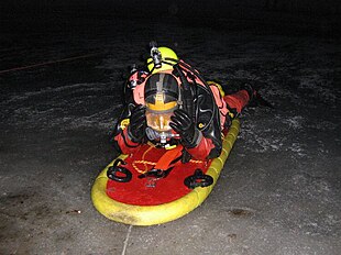 A diver wearing a dry suit skidding on the ice surface, on a special platform, at night.