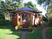 Photographie d'une maison circulaire fabriquée en bois et surmontée d'un toit en pente.