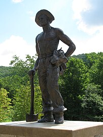 Outdoor statue of a young man standing in work clothes with and axe in his right hand