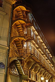 Façade d'un élégant édifice de la Belle Époque avec escaliers extérieurs, photographiée de nuit