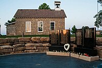 Small memorial of black granite with a one-room schoolhouse in background