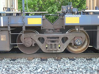 Closeup of a shared bogie with 4 specially adapted side bearings and an articulated connector between two sections of an articulated well car. The roller bearings are not enclosed by an axle box.