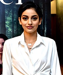 Banita Sandhu wearing a white blouse, looking directly at camera with slight smile