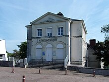 Photographie en couleurs d'un bâtiment carré à étage dont la façade s'orne d'un fronton triangulaire et d'une inscription « Médiathèque ».