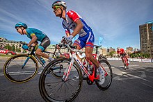 Au premier plan, image de deux coureurs cyclistes en train de pédaler en danseuse, un autre coureur fait de même en arrière-plan.