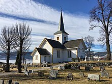 Foto einer weißen Holzkirche mit Grabsteinen im Vordergrund