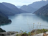 Narrow lake extending toward the background between forested mountains