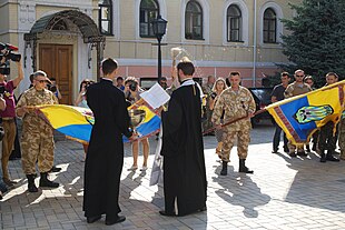 Two priests blessing two flags outside a church