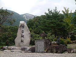 推定地に建つ帰雲城趾の碑。背後に帰雲山の山体崩壊跡が見える。2010年（平成22年）撮影。