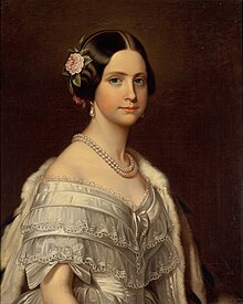 Half-length painted portrait of a young woman wearing a white satin ball gown trimmed with bows and lace, and also wearing an ermine stole thrown over one shoulder, a double strand of large pearls around her neck, pearl drop earrings, and a pink camellia arranged in the hair over her right ear.