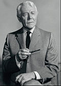 A black-and-white photograph of a man in a suit and tie with white hair and a pipe