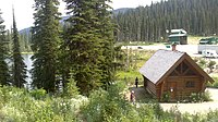 A lake cabin near a lake, with a parking lot and dirt road behind the cabin