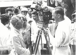 Henk Alsem, in de vooroorlogse jaren een bekende Nederlandse film- en documentairemaker. Charlie Chaplin bekijkt Henk Alsems 35mm-filmcamera op Tanjung Priok Wharf nadat de komiek in de haven van Batavia (later Jakarta) is aangekomen. Chaplin was zelf een verwoed amateurfilmer en hij had zijn eigen 16mm-camera. (1931)