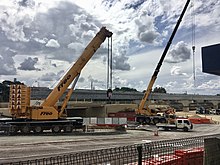 Concrete bridge beams running across road with two mobile cranes in front