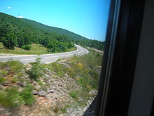 A view of a road from a side, showing two traffic lanes of a single carriageway as the road follows a left curve