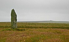 A photograph of a stone standing upright on the left in a field