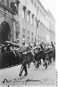 Medlemmer fra det tidlige Hitlerjugend marsjerer taktfast under tiårsmarkeringen av nazistenes «ølkjellerkupp» i München. «Hitlerungdommen» og uniformerte partimedlemmer hilser hverandre med «romersk hilsen». Foto: Deutsches Bundesarchiv