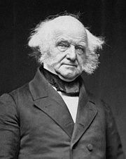 Half-length photographic portrait of an elderly, balding man dressed in a dark coat, vest and cravat