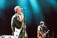 A color photograph of Noel and Liam Gallagher of the band Oasis on stage