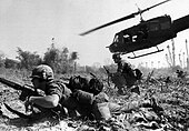 A black and white image of a man crawling across the ground with a helicopter flying in the background