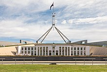 A large white and cream coloured building with grass on its roof. The building is topped with a large flagpole.