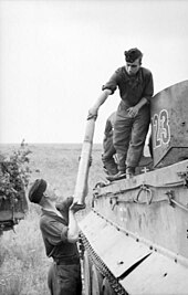 Photographie en noir et blanc montrant un homme passant un obus à un autre homme debout sur un char.