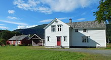 Ein großes weißes Holzhaus im skandinavischen Stil, links daneben eine kleinere rote Hütte und ein Schuppen.