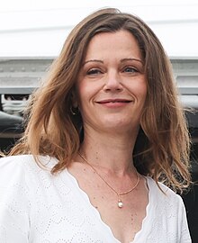 Headshot of a woman with light brown hair, wearing a white dress, and smiling as she boards a plane.