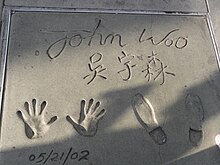 A hand and shoe print reading "John Woo" at the top, the Chinese name "吳宇森" in the middle, and "5/21/2002" at the bottom.