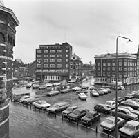 De Nieuwmarkt in gebruik als parkeerterrein voor auto's. Op de achtergrond links gebouw Flesseman, daarnaast de Sint Antoniesbreestraat, gezien vanaf de Waag (links); 1976