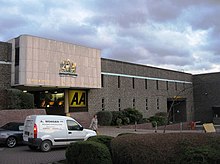 brown brick two storey building with narrow slit windows and gold crest above entrance area