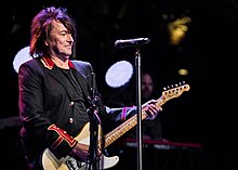 A photograph of Richard Sambora playing guitar on stage during a concert.