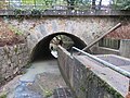 photo d’un pont sous lequel passe une eau boueuse ; au milieu du passage, dans le sens de l’eau, se trouve un mur ; la partie droite est normalement un passage pour les piétons