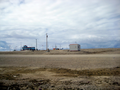 Igloolik Airport at a distance (blue building). A Canadian North airplane arrives, as All-terrain vehicles and trucks drive up to the airport.